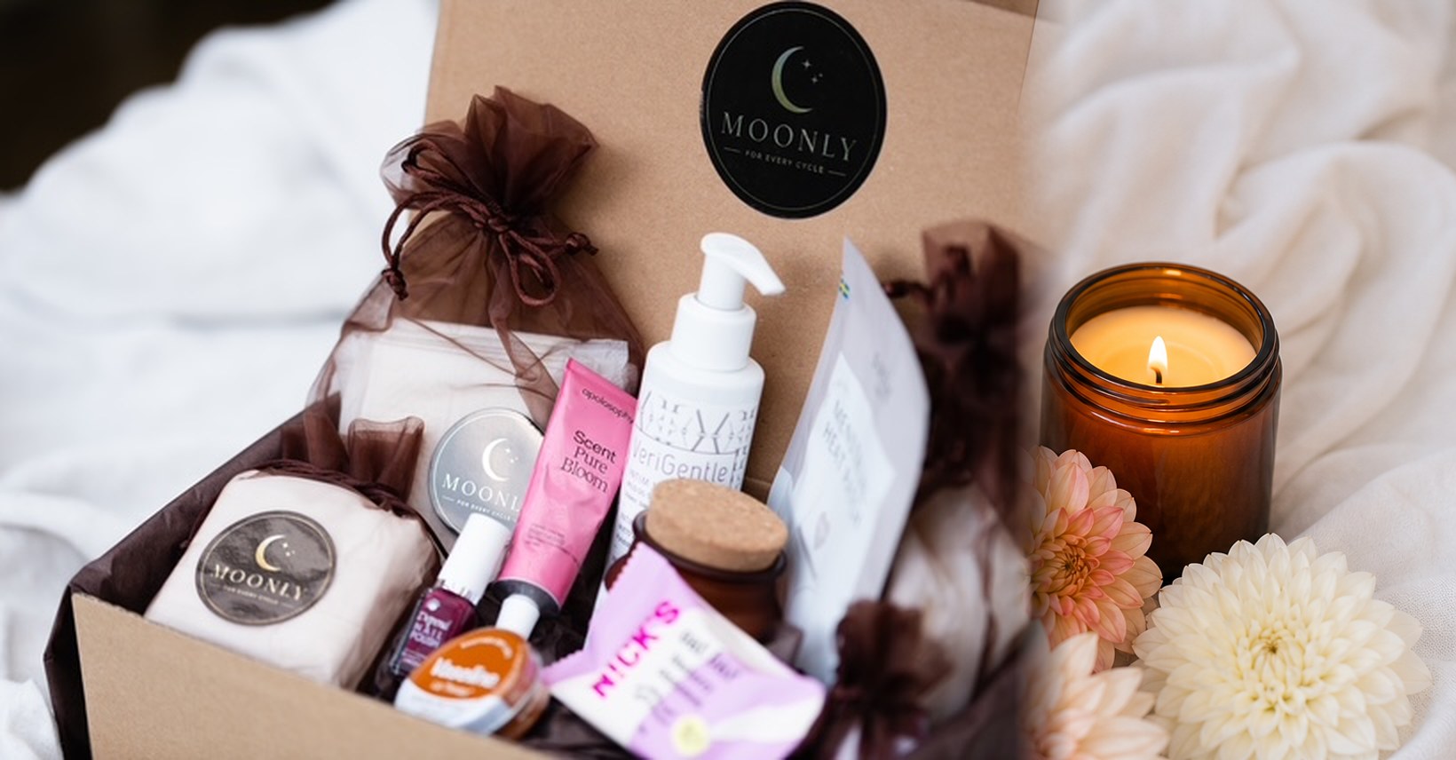 Moonlys mensbox fylld med selfcare-produkter, med ett brinnande doftljus och blommor bredvid